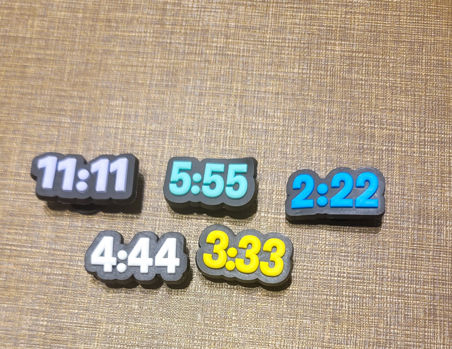 A collection of shoe charm buttons with different angel number designs on a textured background.
