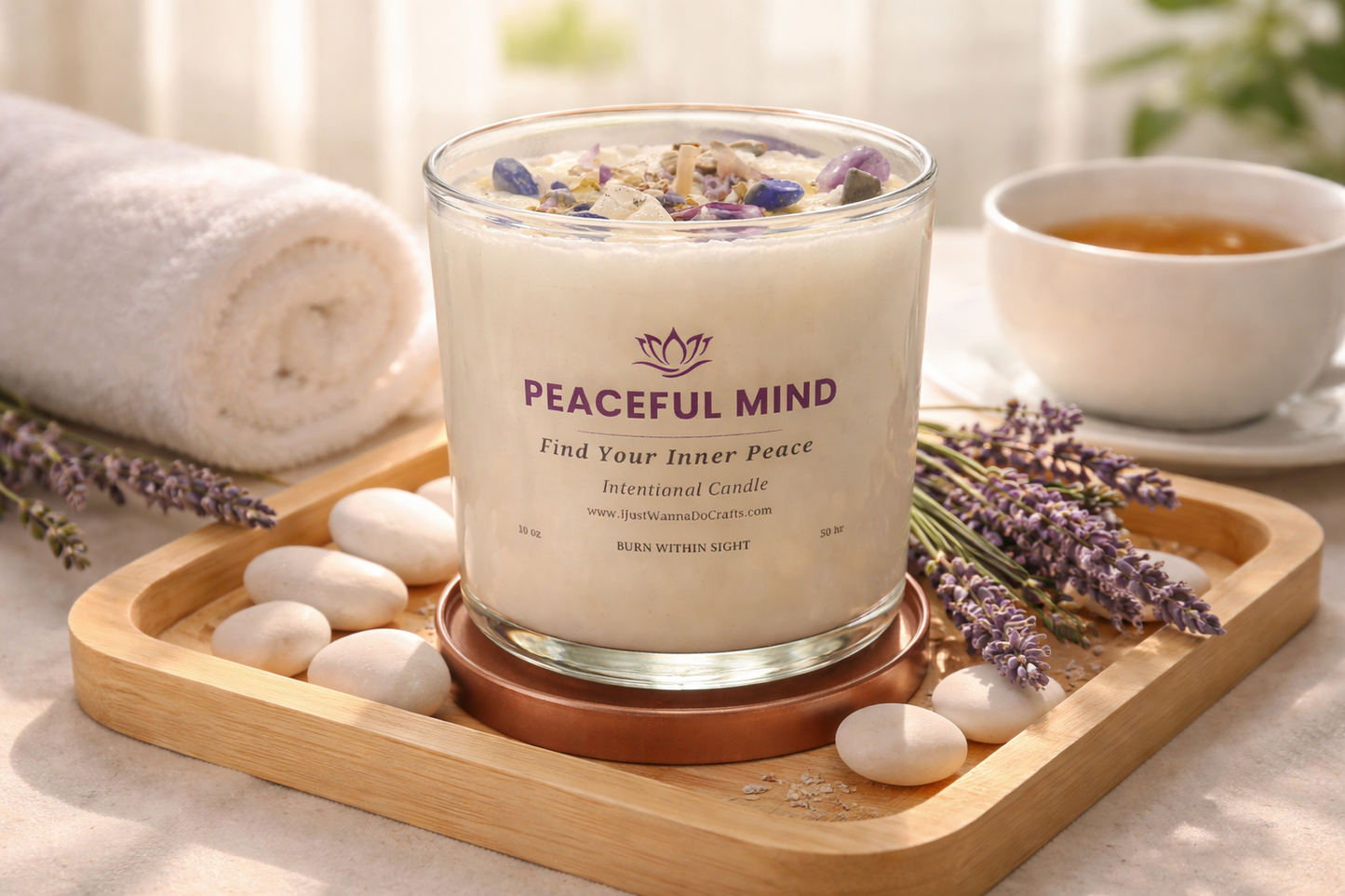 Candle labeled 'Peaceful Mind' on a wooden tray with lavender and stones, next to a tea cup.